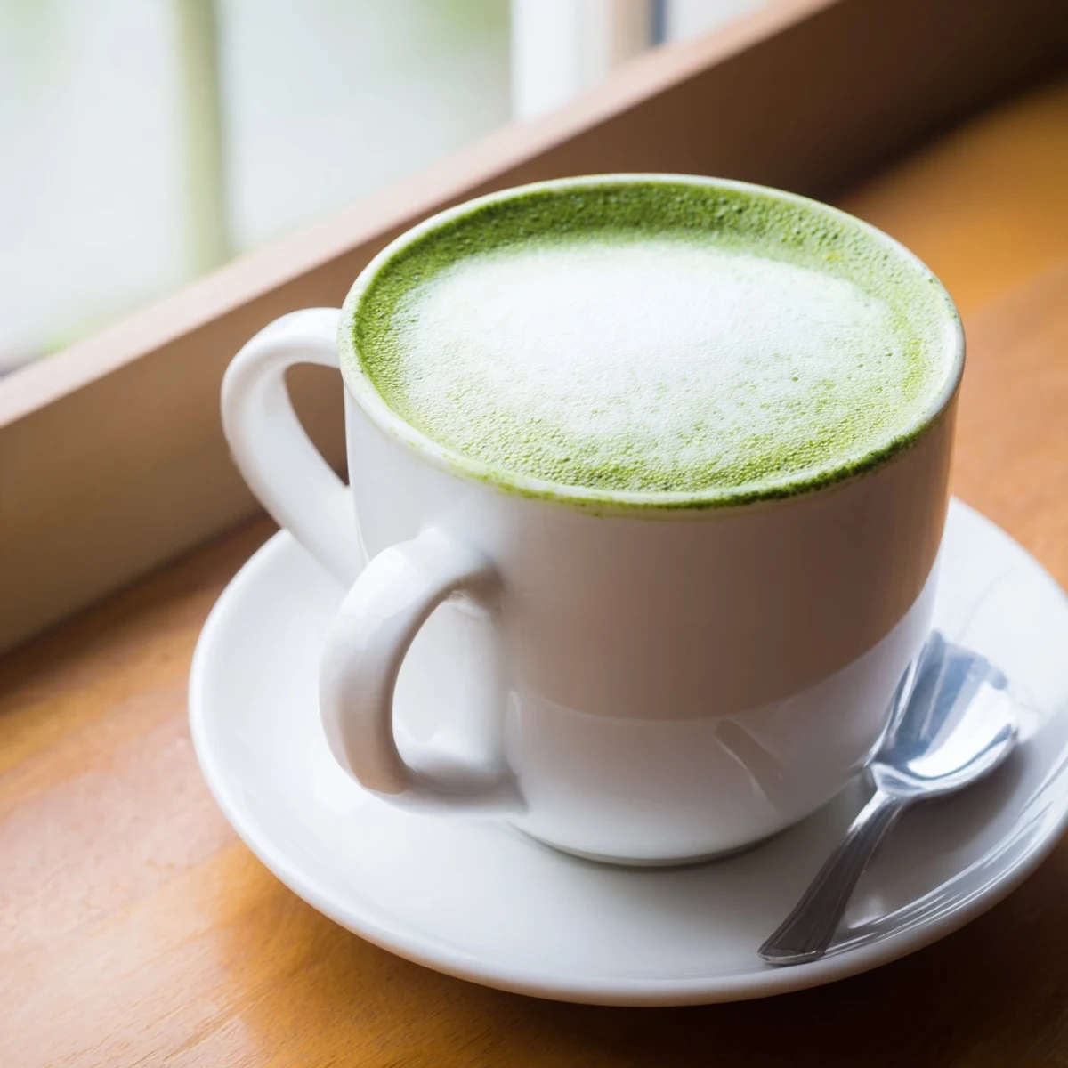 Steaming green tea latte topped with delicate foam in a clear glass mug, showcasing vibrant matcha.
