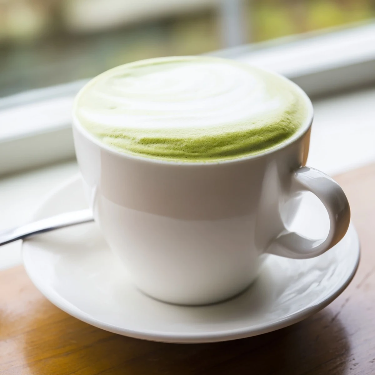 Creamy matcha latte with a dusting of green tea powder served hot beside a book.