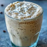 Creamy vanilla bean frappuccino protein shake with whipped cream and vanilla bean specks in a tall glass.