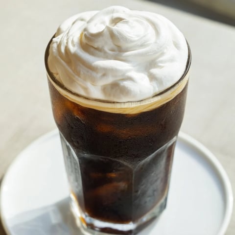 Fluffy, cloud-like Starbucks cold foam swirls on top of a dark iced coffee, ready to enjoy.