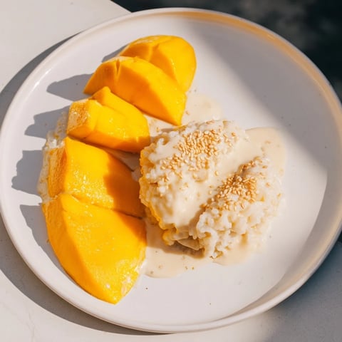 Golden mango slices alongside creamy Thai Mango Sticky Rice, drizzled with coconut sauce.