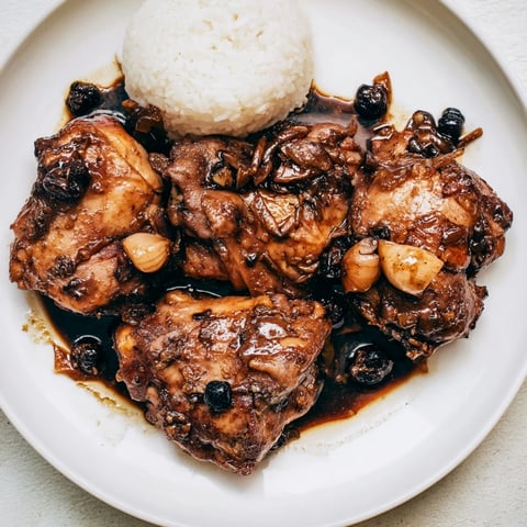 Tender Filipino Chicken Adobo, glistening with sauce, served over fluffy white rice for a flavorful meal.