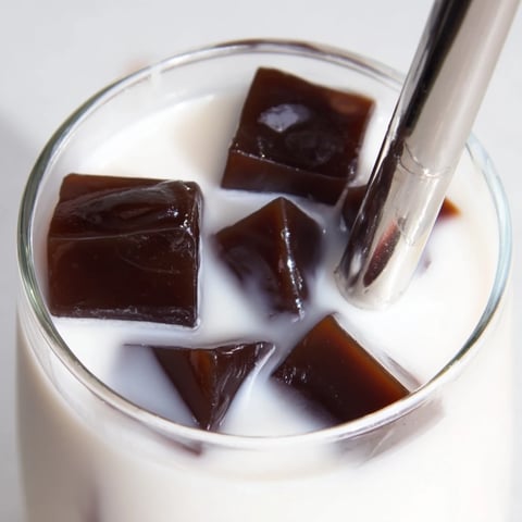 Creamy milk and bouncy Coffee Jelly Drink cubes fill a clear glass over ice.