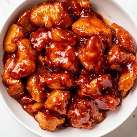 A steaming bowl of Sweet Chili Chicken with fluffy jasmine rice and bright green steamed broccoli, garnished with sesame seeds and fresh green onions.