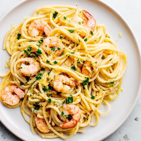 A close-up of Lemon Garlic Shrimp Pasta in a white bowl, showing juicy pink shrimp and spaghetti coated in a glossy, lemon-garlic butter sauce with fresh parsley.