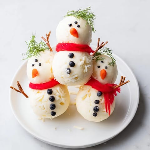 This snowman cheese ball trio, a fun holiday appetizer, is presented on a platter with colorful garnishes.