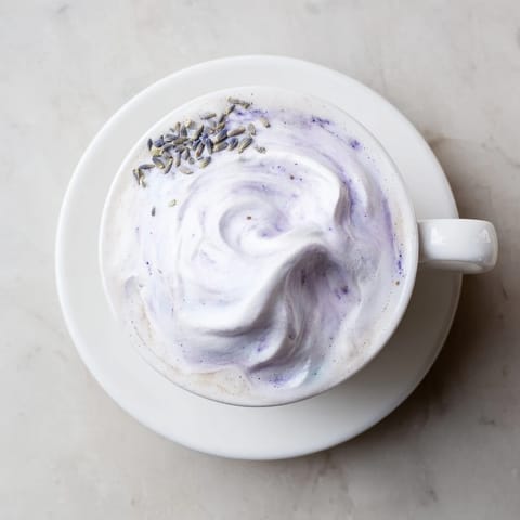 A close-up of a Whipped Lavender Latte garnished with dried lavender buds beside a scone.  