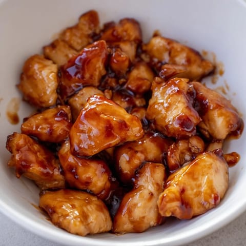 Close-up of tender chicken pieces coated in a glossy, tangy-sweet chili glaze, paired with vibrant broccoli florets on a bed of white rice.