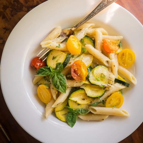 A vibrant bowl of Garden Veggie Pasta, finished with fresh basil ribbons and optional Parmesan, glistening with a light pan sauce.  