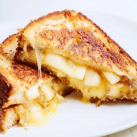 Two halves of Smoked Gouda & Apple Grilled Cheese, melty cheese strings and buttery bread beside fresh apple slices.