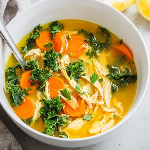 Close-up of High Protein Lemon and Turmeric Chicken Soup, garnished with fresh parsley and lemon wedges, served in a rustic bowl. 