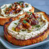 Creamy white bean and roasted garlic spread generously slathered on crisp sourdough toast, garnished with fresh herbs for a savory appetizer.