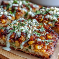 Crispy flatbread topped with charred street corn, cotija cheese, and zesty jalapeño crema for a festive Cinco de Mayo dish.  